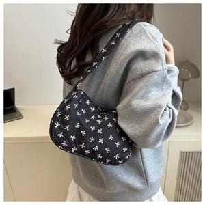 Detail of black hobo bag with pink bow pattern on a model in a minimal home setting