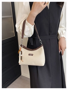 Detail of canvas crescent shoulder bag with brown leather trim and beaded charm accessory