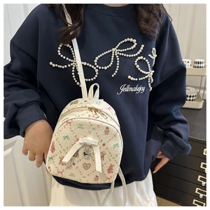 Detail of a creamy white mini backpack with cute bear prints and a 3D bow accent