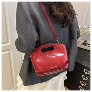 Detail of red patent leather bucket bag with top handle and fashion text on a grey suit