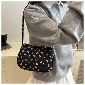 Detail view of black underarm bag with pink bow pattern and quilted texture on model