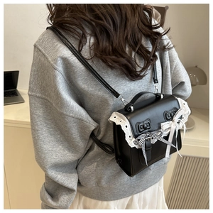 Detail of black PU bag featuring white lace edges and decorative bow on the back