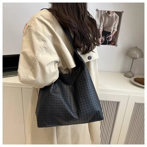 Détail d'un sac cabas noir en cuir tressé porté par un mannequin en trench-coat beige