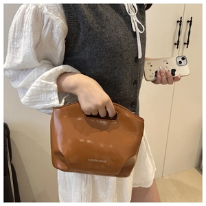 Brown glossy leather dumpling bag with white lettering held by a model in a minimal room