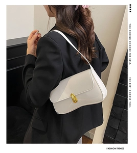 Close-up of a white leather underarm bag with gold oval buckle worn with a black blazer