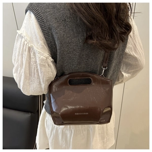 Detail of dark brown patent leather bucket bag with top handle and fashion logo engraving