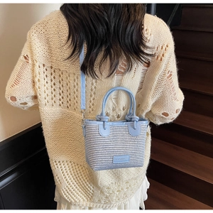 Detail view of light blue woven bucket bag with leather strap on a model with knitwear