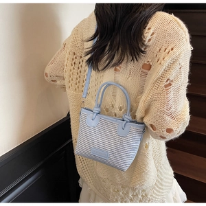 Detail of light blue woven bucket bag with fashion label and textured top handles