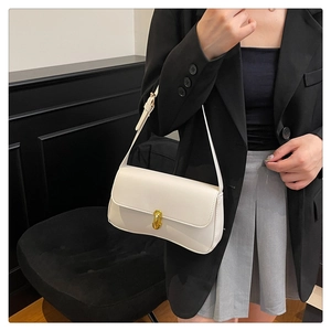 Chic cream small square bag with gold lock buckle worn over shoulder on a black blazer