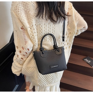Detail of black straw woven handbag with knot handle and Fashion tag on beige knit dress