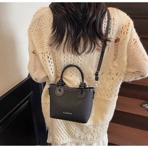 Detail of black woven texture mini bag with metal plate and leather strap over beige knit