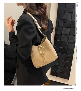 Gros plan du sac beige avec boucle dorée ondulée et détail élégant de pompon décoratif