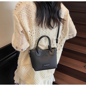 Detail of a black woven bucket bag with fashion label and textured synthetic leather