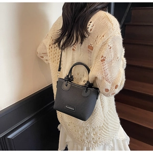 Detail of black woven bucket bag with Fashion tag held by model on wooden stairs