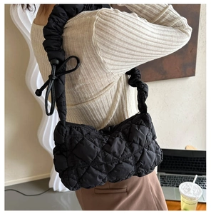 Detail of black quilted shoulder bag featuring ruffled handle and bow decoration