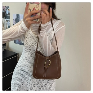 Détails d'un sac porté épaule en cuir marron avec surpiqûres blanches et boucle dorée