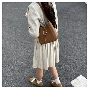 Brown leather hobo bag with white stitching, gold buckle, and tassels worn by a model