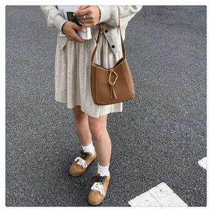 Detail of a brown leather shoulder bag with white contrast stitching and a gold metal buckle