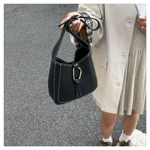 Detail of black leather bucket bag with white contrast stitching and gold ring buckle