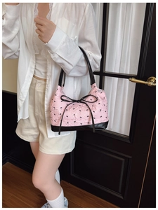 Detailed close-up of pink jacquard handbag with black bows shown on model's shoulder