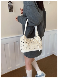 Detail of cream shoulder bag with wave texture and black bow patterns on model