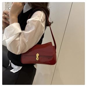 Detailed view of deep red patent leather shoulder bag with gold metal clasp on model