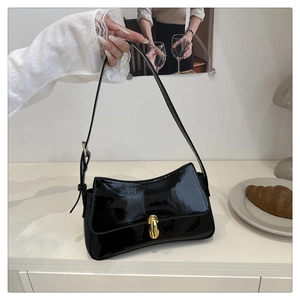 Detail of black patent leather handbag with gold twist lock on a minimalist white desk