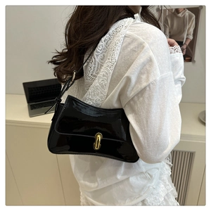 Close-up of a black patent leather baguette bag with a gold buckle worn on the shoulder
