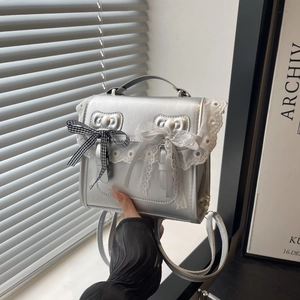 Silver flap backpack with lace trim and double bows, worn as a crossbody handbag