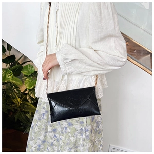 Chic black envelope crossbody bag with gold chain strap shown on a floral skirt outfit