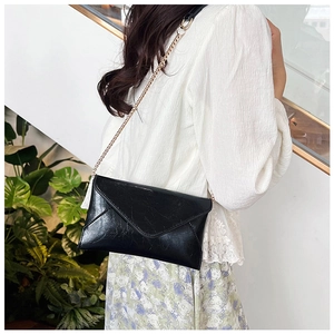 Detail of a chic black envelope crossbody bag with a gold chain strap on a female model