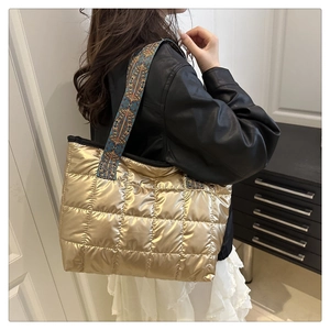 Détail d'un sac cabas doré matelassé avec une large bandoulière à motif ethnique
