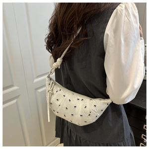 Detail of white dumpling bag featuring black bow embroidery and woven shoulder strap knots