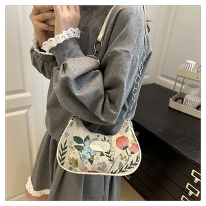 Close-up of vintage floral embroidery and leather chain strap on ivory crescent bag