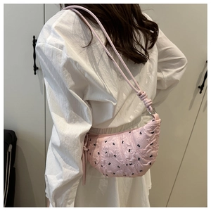 Detail of pink dumpling bag with 3D texture and black bow accents on a model