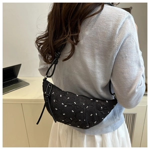 Detailed side view of black crescent bag with white bow embroidery on a female model