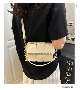 Détail d'un sac à bandoulière tressé crème avec bords festonnés et chaîne dorée chic