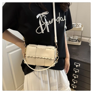 Detail of cream woven crossbody bag featuring scalloped edges and gold chain accent