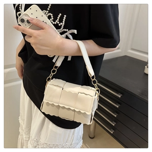 Détail du sac bandoulière en cuir beige tressé avec bords festonnés et chaîne dorée