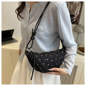 Detail of black croissant bag featuring white bow patterns and elegant pleated texture