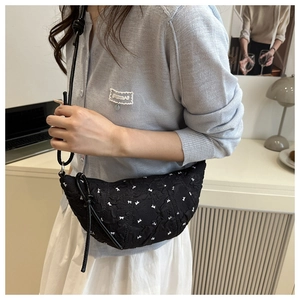 Detail of black crescent shoulder bag featuring white bow patterns and quilted texture