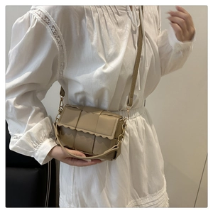Detail of light khaki woven crossbody bag with wavy edge flap and gold chain strap