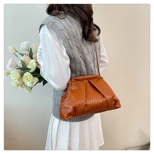 Chic orange pleated cloud bag worn as a shoulder bag on a female model with a gray vest