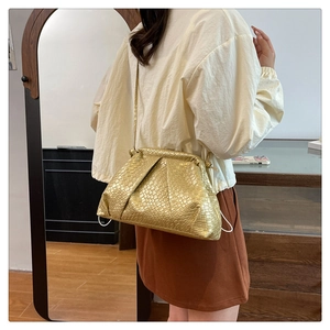 Detail of golden woven dumpling bag texture and slim leather shoulder strap on a model