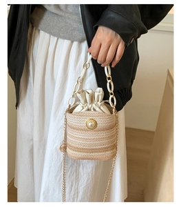 Detail of woven straw bucket bag showing pearl clasp, drawstring and gold chain strap