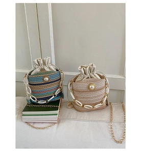 Detail of straw bucket bags with pearl buttons and metal chain straps on books