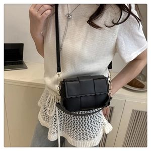 Gros plan d'un sac bandoulière tressé noir avec chaîne décorative et bordure ondulée