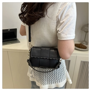 Close-up of black woven leather texture and wavy edge flap on a small shoulder bag