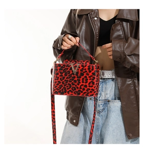 Detail of red and black leopard print crossbody bag featuring a golden V-shaped metal buckle
