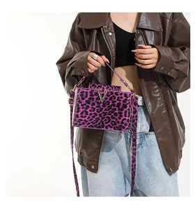 Detail of purple leopard print crossbody bag with gold V-buckle on brown leather jacket